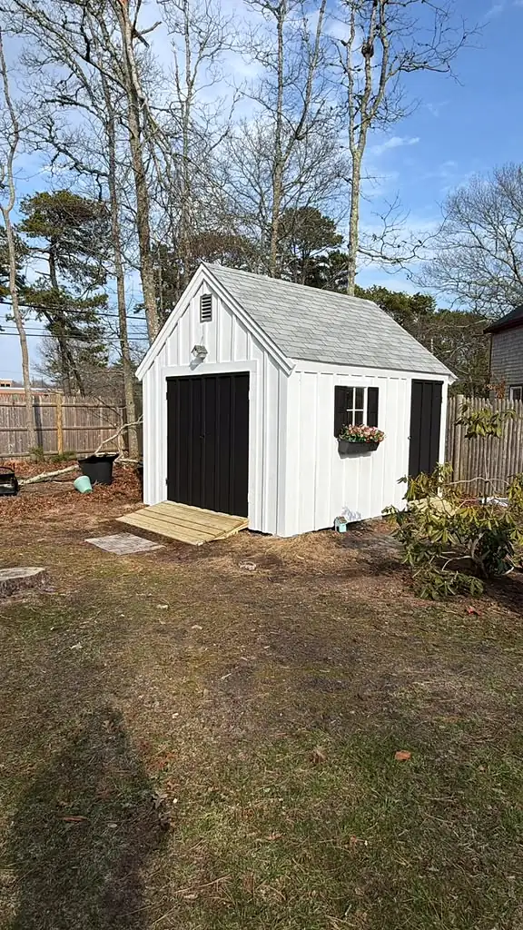 After: the garden shed restored, with white board-and-batten siding, black doors and a flower box